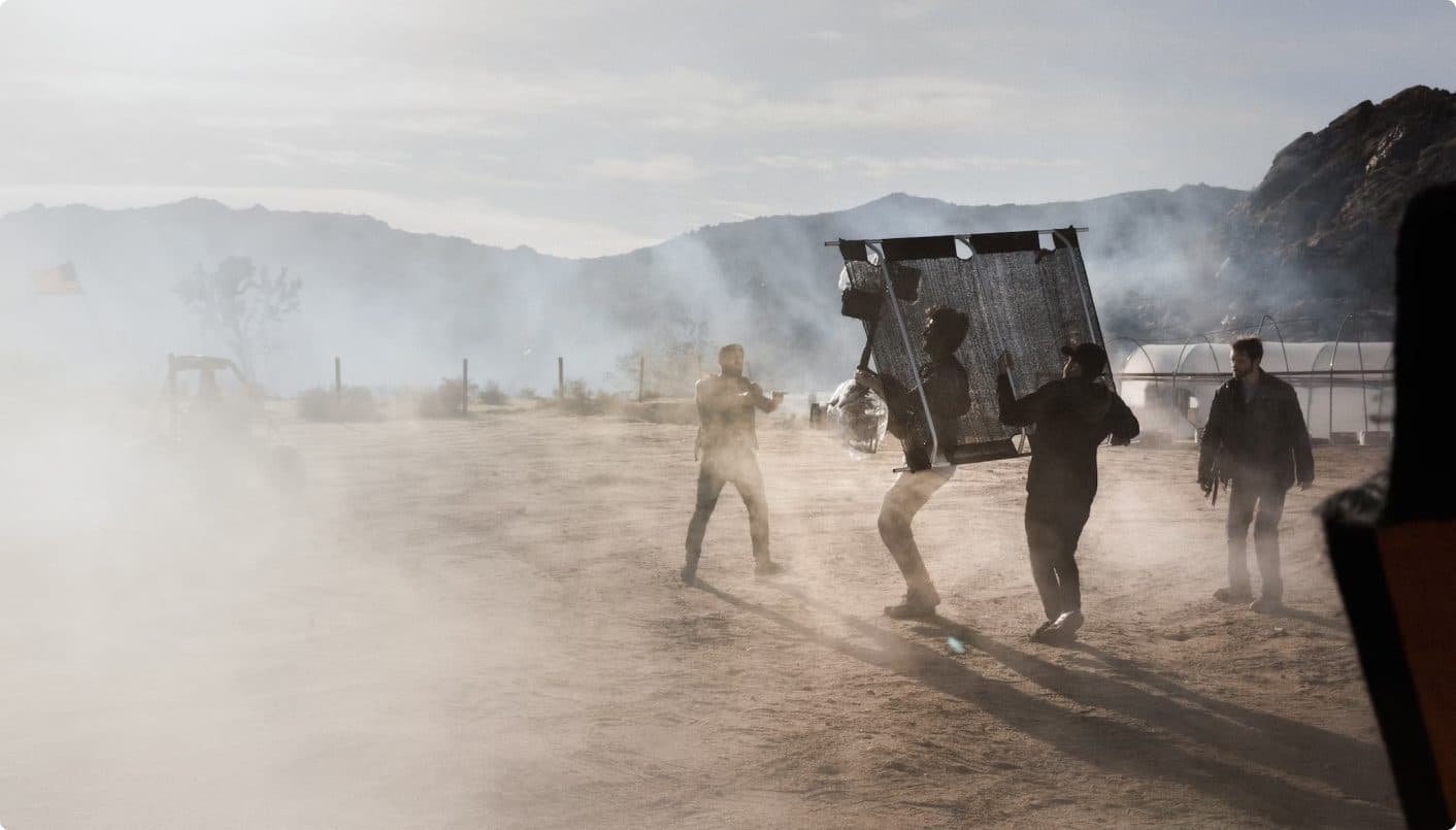 Film crew carrying a lighting rig on a dusty location set